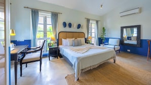 A bedroom with a bed, a desk, a chair, a mirror, and a window with curtains. - ELIVAAS Elysium 3BHK Villa With Jacuzzi (Anjuna)