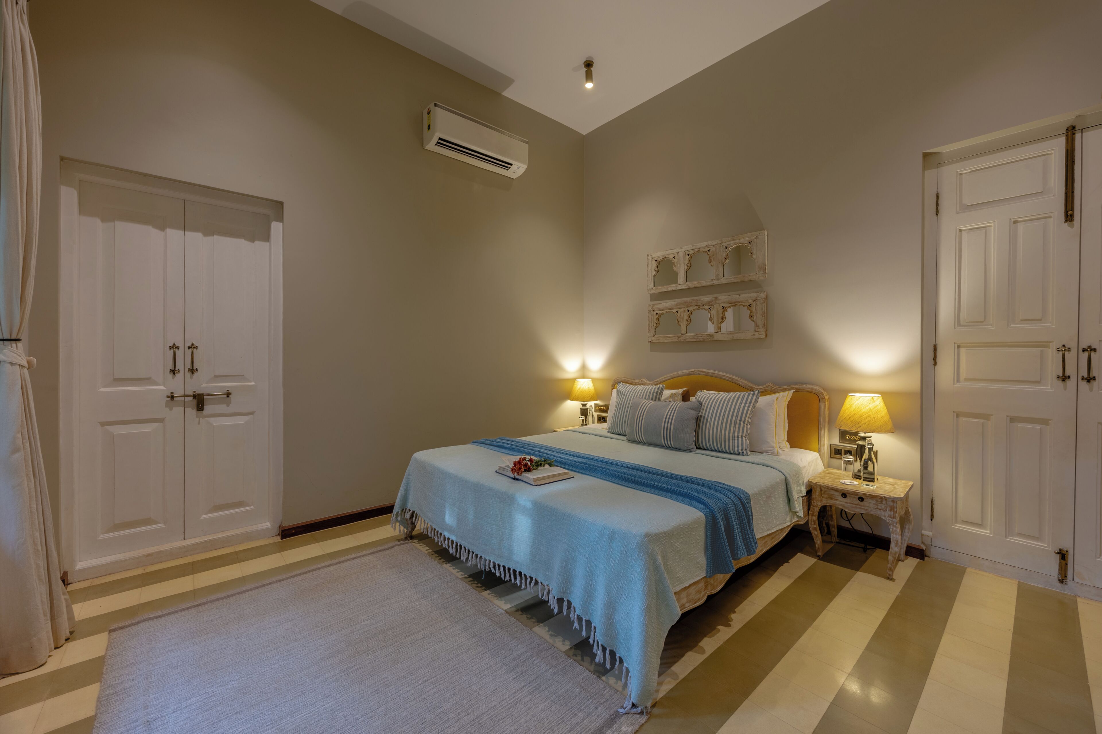 A bedroom with a bed, bedside tables, an air conditioning unit, and a wardrobe.
