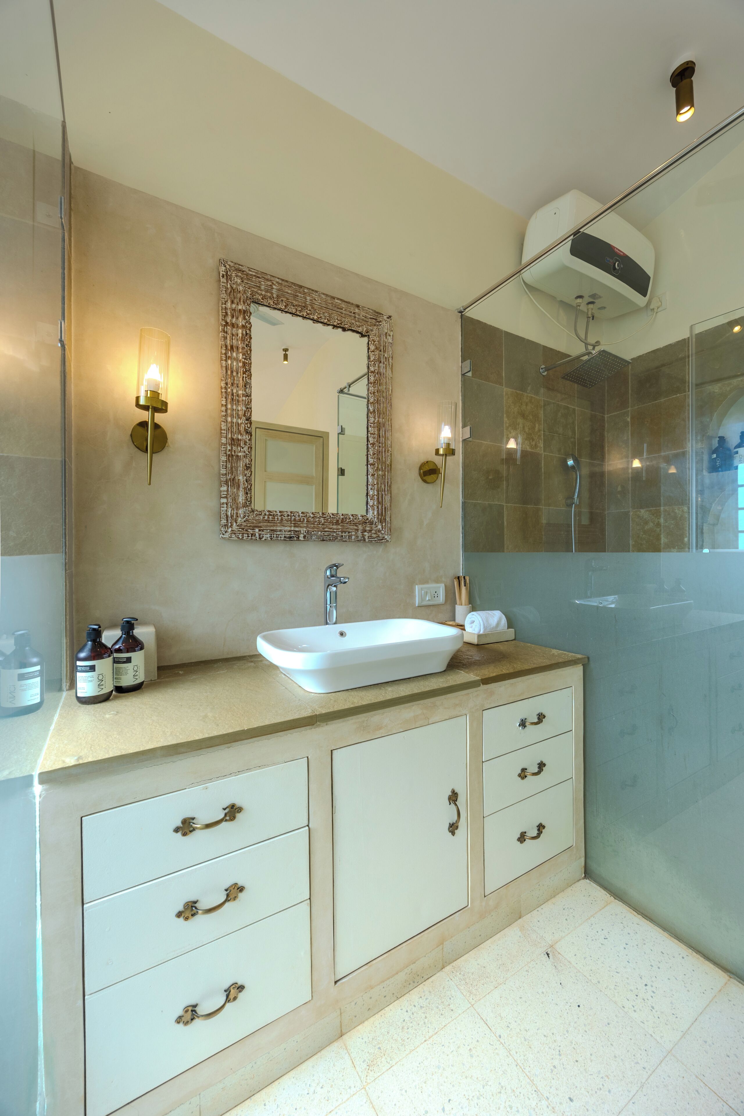 Une salle de bain avec un lavabo blanc, un miroir doté d’un cadre décoratif, une douche avec des portes en verre et un climatiseur fixé au mur.