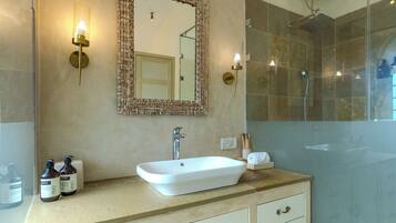 Une salle de bain avec un lavabo blanc, un miroir doté d’un cadre décoratif, une douche avec des portes en verre et un climatiseur fixé au mur.