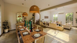A spacious living area with a dining table set for four, a sofa, and a kitchen area in the background. - ELIVAAS Elysium 3BHK Villa With Jacuzzi (Anjuna)