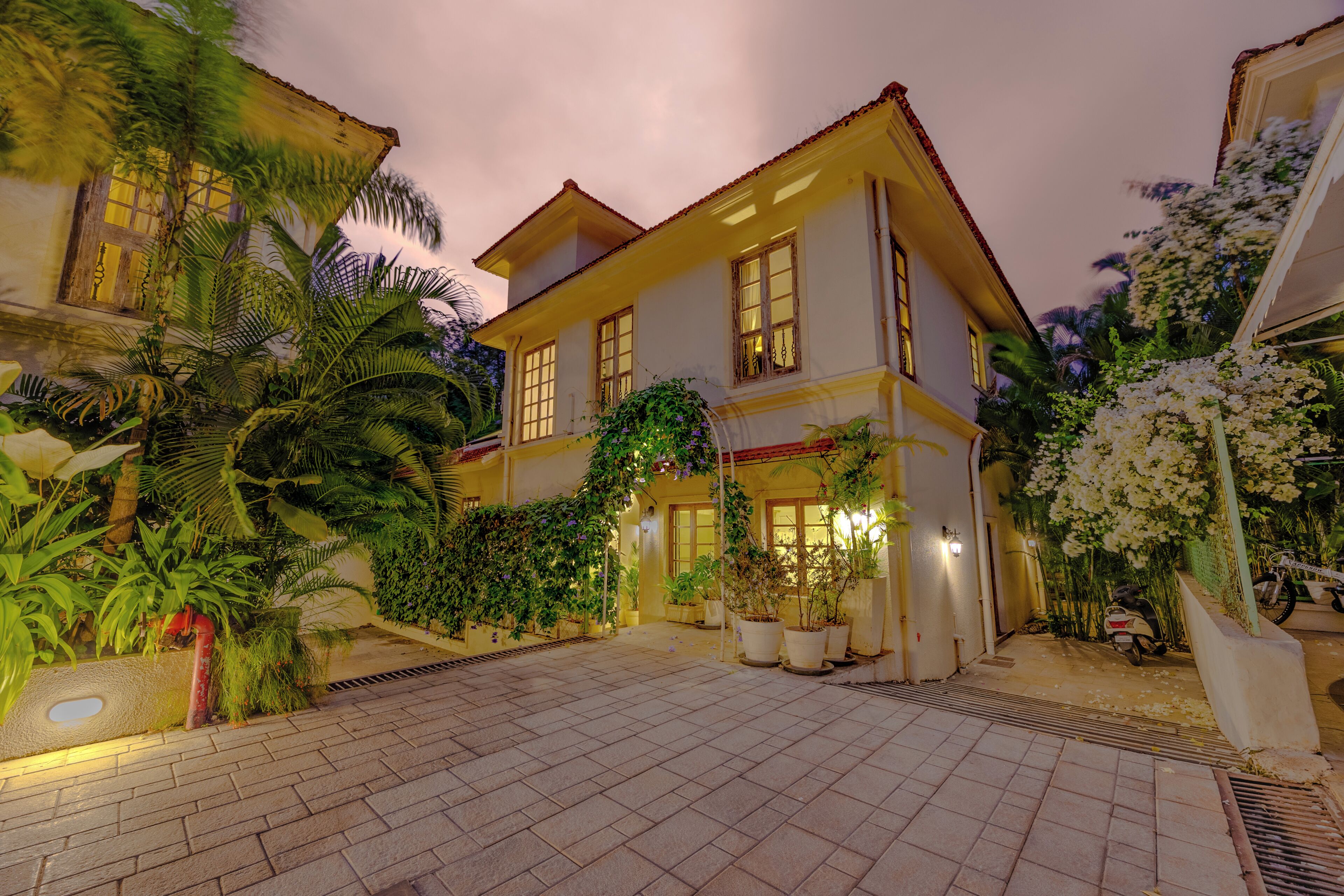 A two-story building with a tiled courtyard, potted plants, and a scooter parked outside.