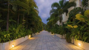 A paved pathway flanked by lush greenery and illuminated by wall-mounted lights. - ELIVAAS Elysium 3BHK Villa With Jacuzzi (Anjuna)