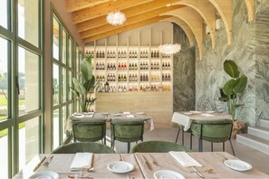 Restaurante com parede de vinhos, teto de madeira e grandes janelas.