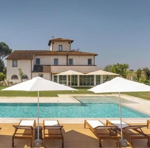 A pool with lounge chairs and umbrellas, a house with a tiled roof, and a clear sky. - Tenuta Asmara Luxury Resort: Garden View Suite (Toscana)