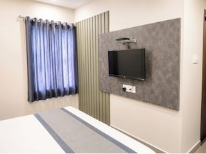 Un dormitorio con cama, televisor montado en la pared y ventana con cortinas.