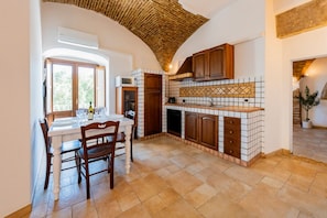 Una cucina con pareti rivestite di piastrelle, mobili in legno, un tavolo da pranzo con sedie e una finestra vista.