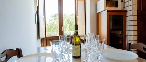 A dining table set with plates, glasses, and a bottle of wine, with a view of greenery outside.