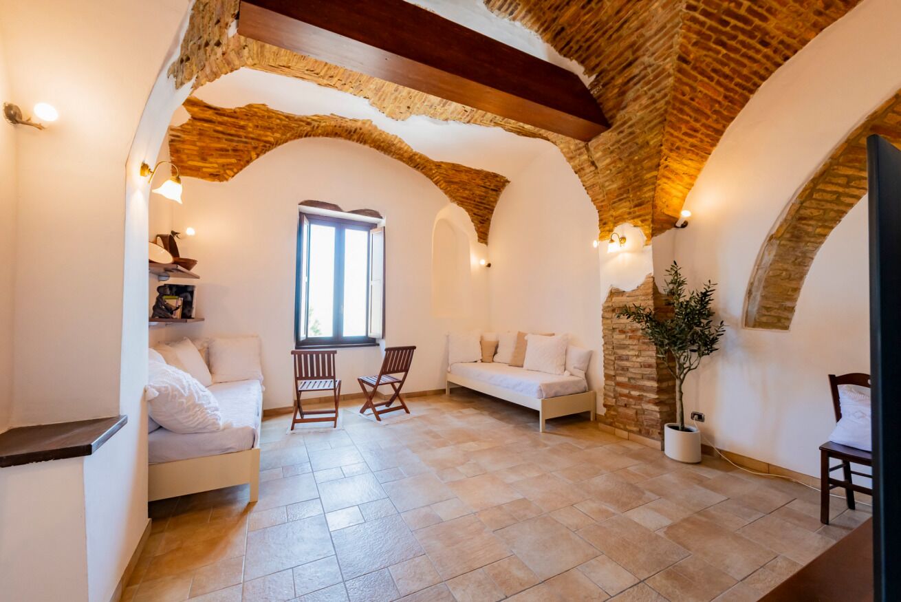 Une pièce avec un plafond en pierre, des murs blancs, un banc en bois, un canapé blanc et une plante en pot.