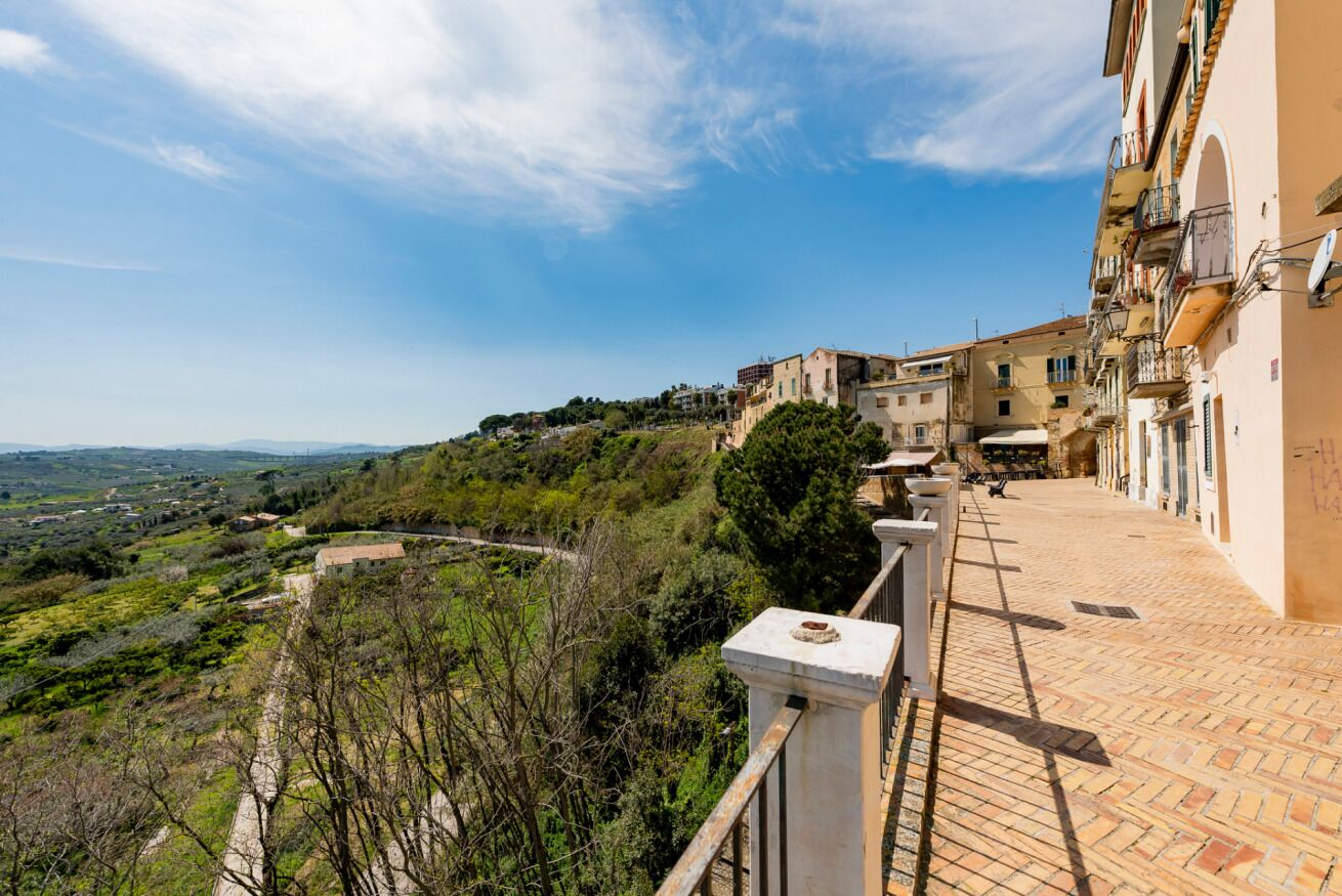 Une ville située sur une colline, avec des bâtiments, une promenade dallée et une vue sur la campagne.