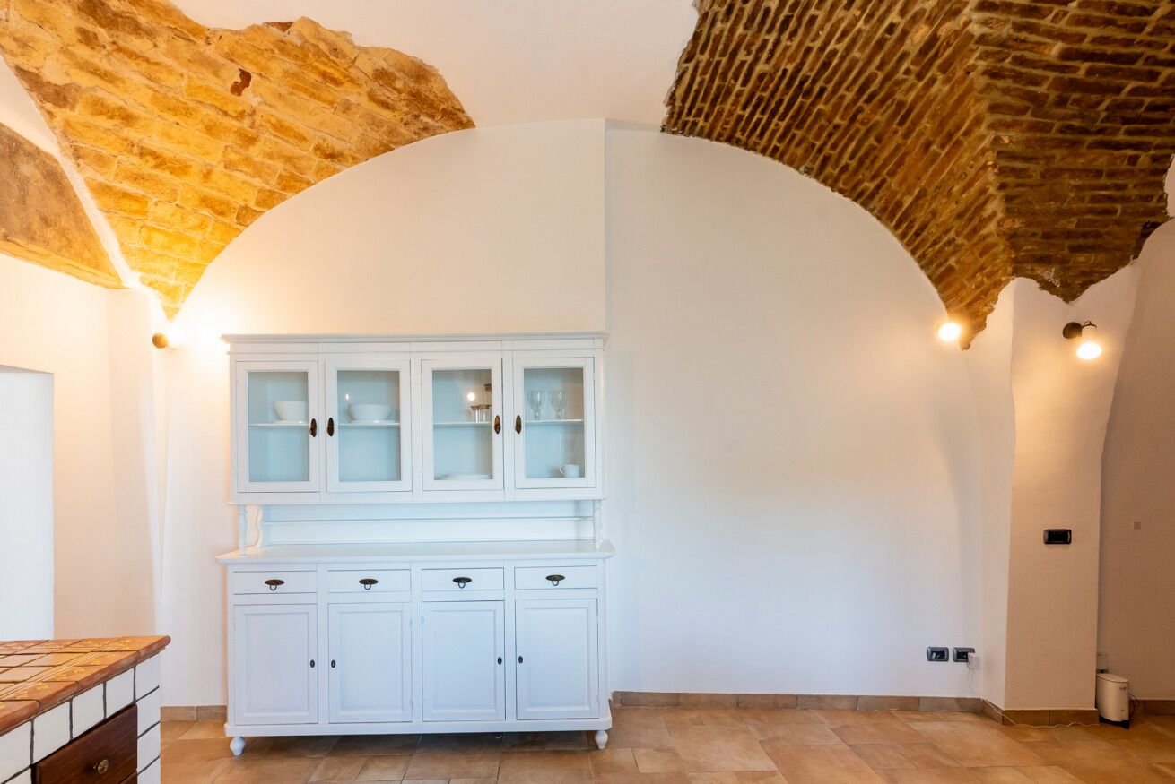 Une pièce avec une armoire blanche, un sol carrelé et des briques apparentes au plafond.
