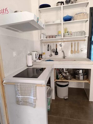 Une cuisine compacte équipée d’une cuisinière intégrée, d’un évier et d’un petit plan de travail. Des étagères situées au-dessus de l’évier servent à ranger la vaisselle et les ustensiles de cuisine.