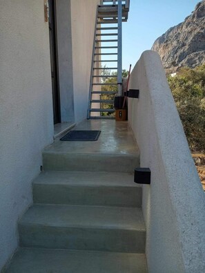 Un escalier en béton avec une rampe métallique menant à une porte, le tout entouré de murs blancs et offrant une vue sur la montagne.