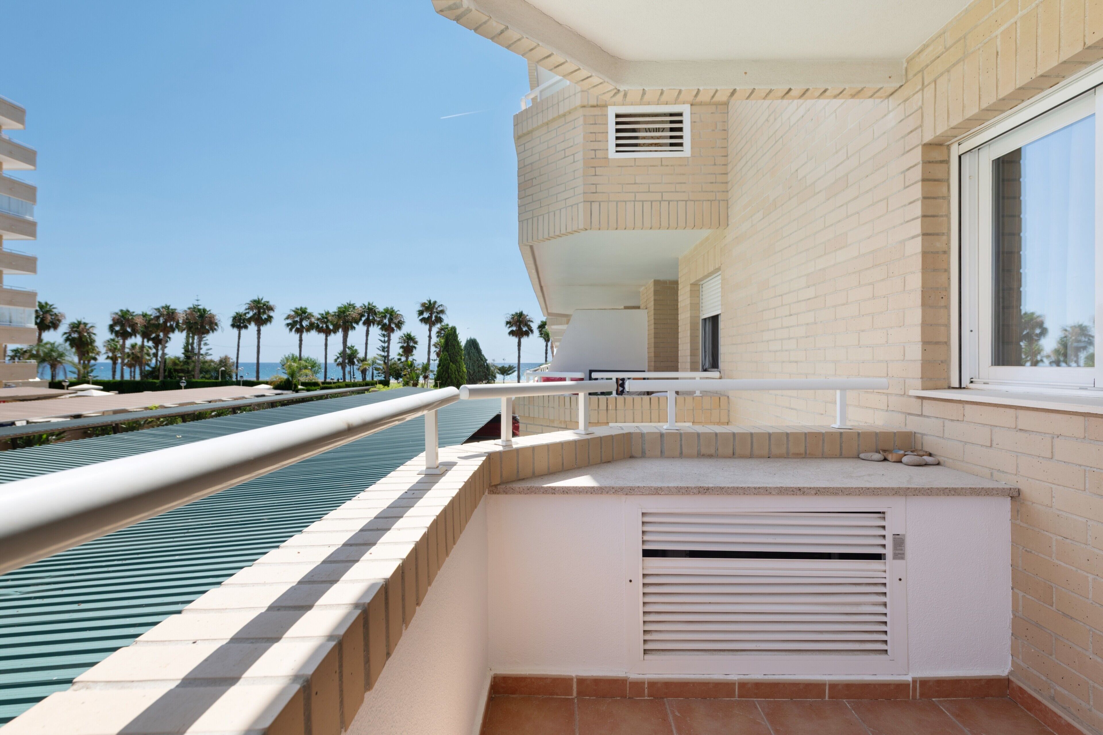 Un balcon avec une piscine, une vue sur les palmiers et un ciel dégagé.