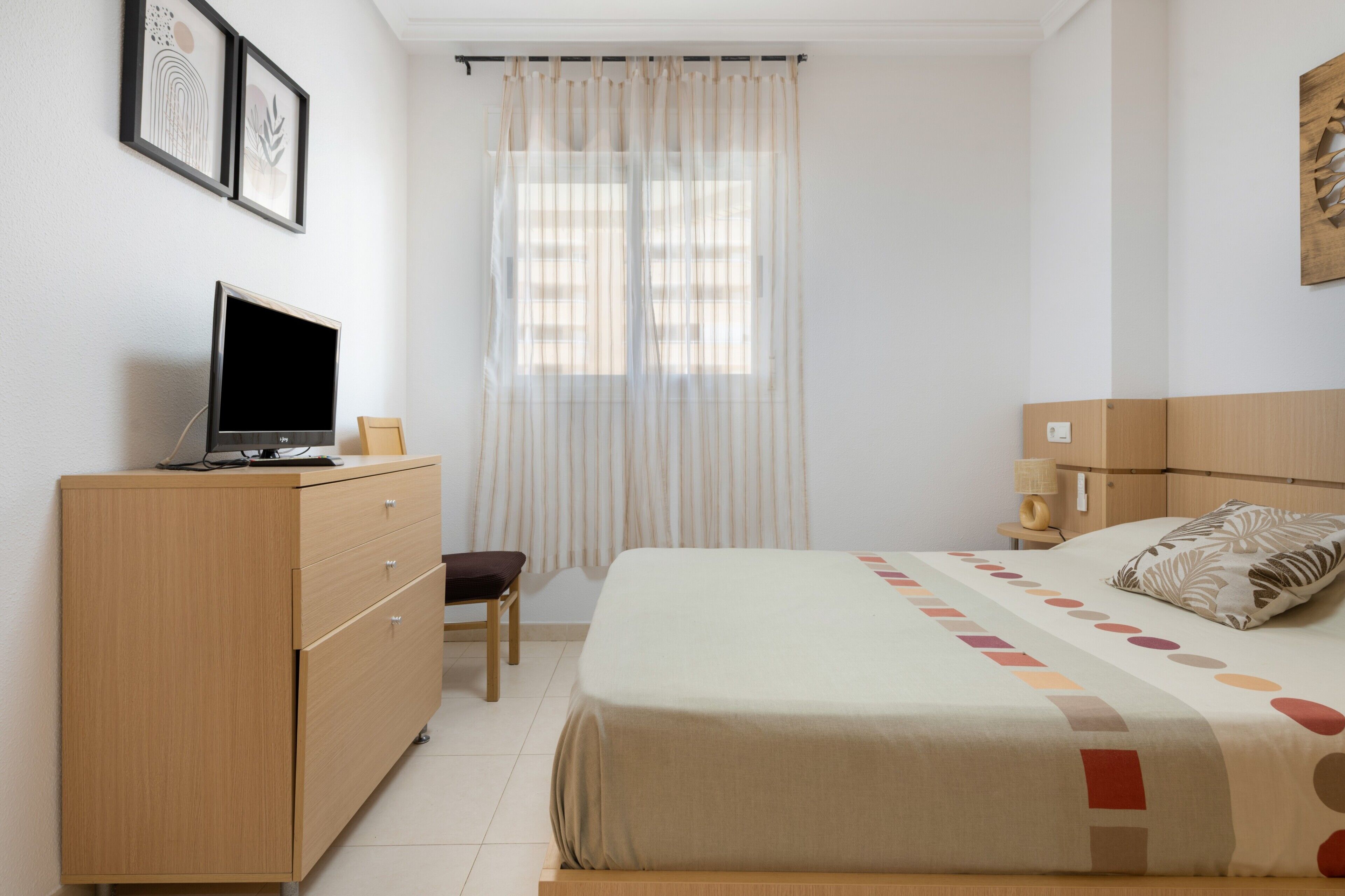Une chambre à coucher avec un lit, un bureau avec un ordinateur, une chaise, une fenêtre avec des rideaux et une lampe fixée au mur.