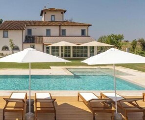 A pool with lounge chairs and umbrellas, a house with a tiled roof, and a clear sky. - Tenuta Asmara Luxury Resort: Deluxe King Suite (Toscana)