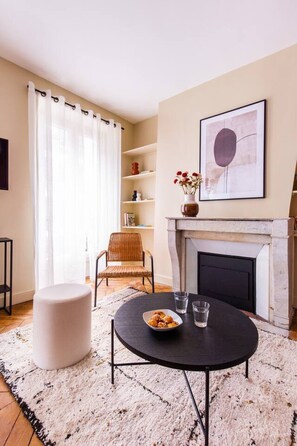 A living room with a fireplace, a round table with a bowl of snacks, a wicker chair, and a white ottoman. - 2. Two bedrooms#Champs-Élysées#Arc de Triomphe#AC (Paris)