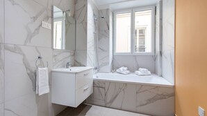 Une salle de bain moderne avec des murs en marbre, un meuble-lavabo à deux vasques, une douche et une fenêtre avec vue.
