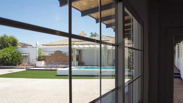 Vista attraverso una finestra su una piscina, un patio e un edificio con tetto in tegole.