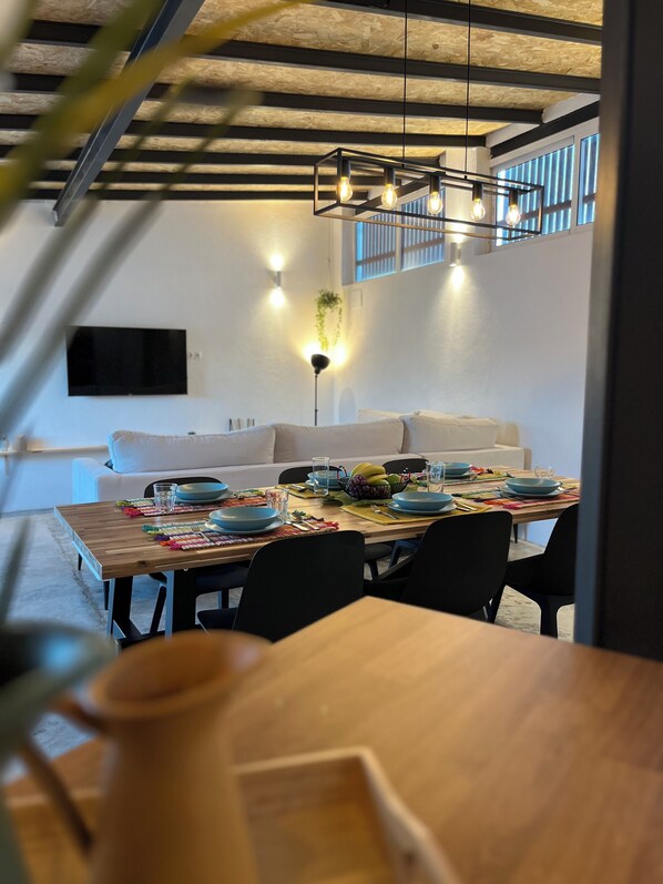 A modern dining area with a wooden table set for a meal, a sofa, and a TV mounted on the wall.