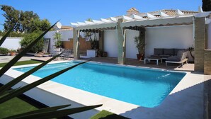 Una piscina con un pergolato, zone salotto all'aperto e piante in vaso.