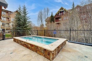 A swimming pool with stone tiles, surrounded by a fence, in a residential area with multi-story buildings and trees. - Luxury condo with hot tubs & pool, walk to lifts & downtown Breckenridge (Breckenridge)