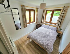 Ein Schlafzimmer mit einem Bett, zwei Fenstern, einem Nachttisch und einer Pendelleuchte.
