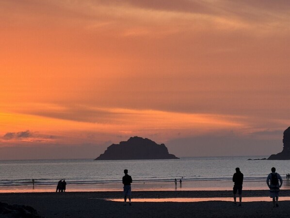 Eine Strandansicht mit Silhouetten von Menschen und einem Hund, einem ruhigen Meer und einem Sonnenuntergangshimmel.