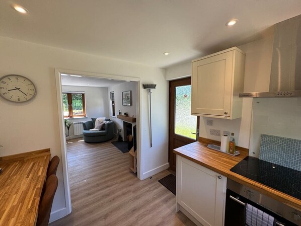 A modern kitchen with a wooden countertop, a built-in stove, and white cabinets. There is a dining area with a wooden table and chairs, and a living room with a sofa and a coffee table.