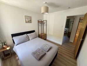 Ein Schlafzimmer mit Bett, Nachttisch, Lampe und Blick ins Badezimmer.