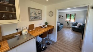 A modern kitchen with a wooden countertop, two bar stools, a kettle, and a clock on the wall.