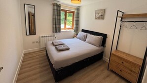 A bedroom with a bed, a window with curtains, a radiator, a wooden dresser, and a hanging clothes rack.