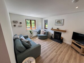 A living room with a sofa, a round seating area, a fireplace, and a TV. - Greenking Cottage A 2 bed sleeps 4 (Trethevy)