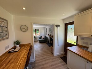 A modern kitchen with wooden countertops, a dining area with a table and chairs, and a living room with a sofa and a fireplace. - Greenking Cottage A 2 bed sleeps 4 (Trethevy)