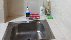 Una cocina con un lavamanos de acero inoxidable, un estante de vidrio con utensilios de cocina y una pared blanca con un diseño decorativo.