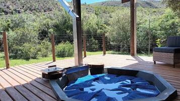 A hot tub on a wooden deck with a view of a hilly landscape.