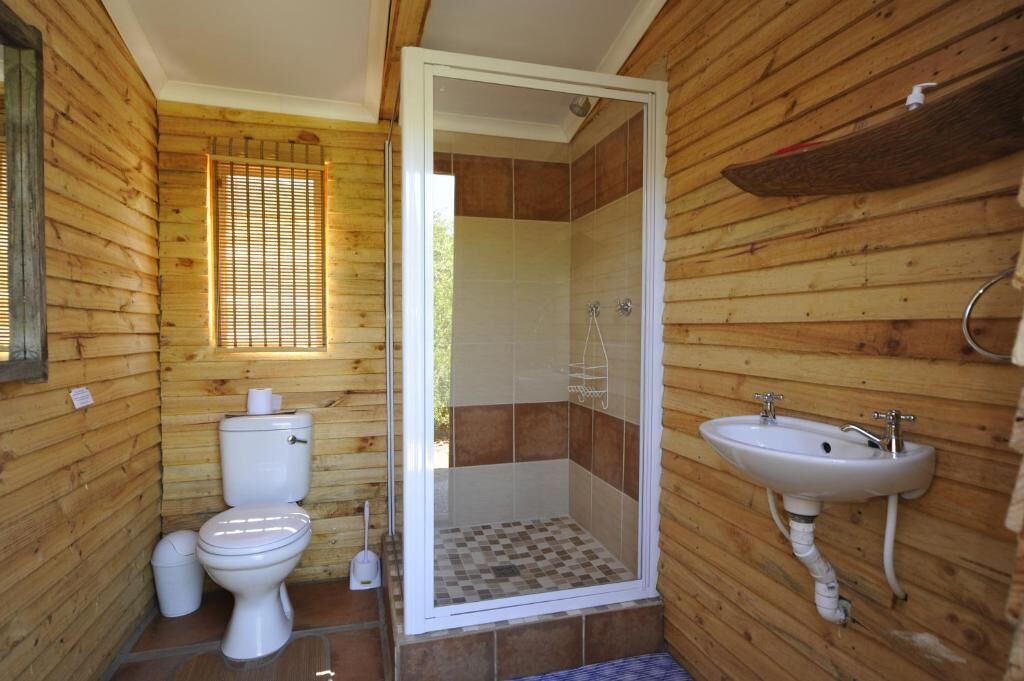 Une salle de bain rustique, aménagée dans une cabane en bois, avec des toilettes, une douche et un lavabo.