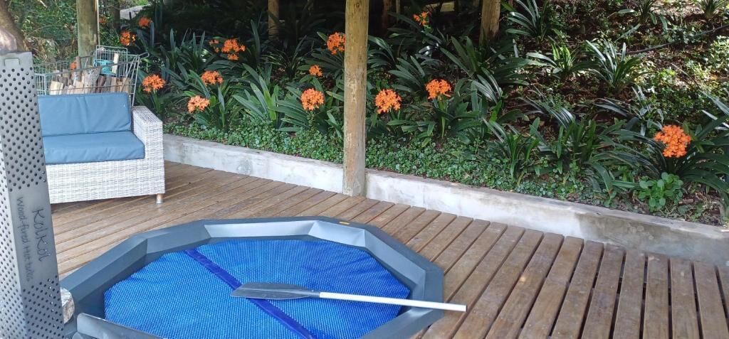 A hot tub with a blue mat, surrounded by a wooden deck and a wicker chair.