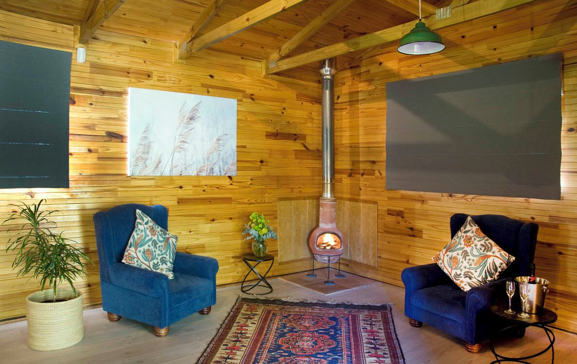 A cozy room with wooden walls, two blue armchairs, a rug, a fireplace, and a painting.