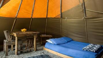 A tent with a bed, a table, and a chair inside.
