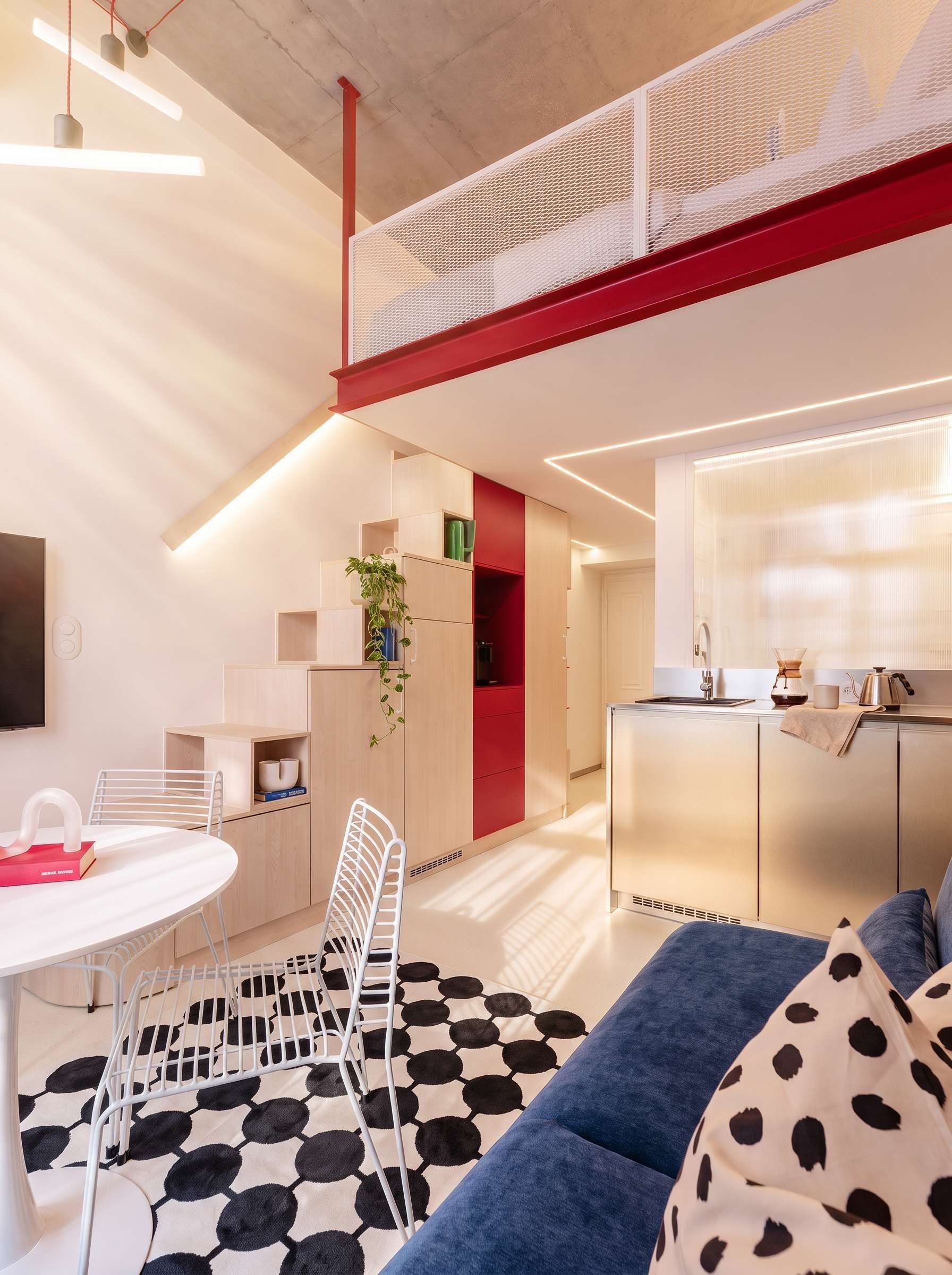 A modern kitchen with a central island, a dining area with a white table and chairs, and a living area with a blue sofa.