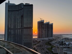 A high-rise building with a curved facade, a construction crane, and a sunset in the background.