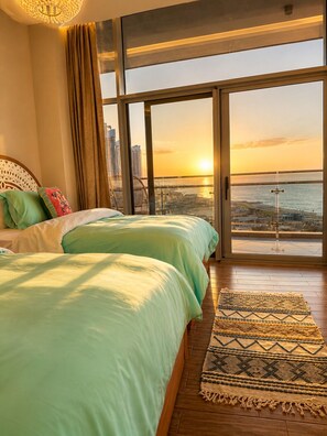 Quarto com uma janela grande, uma cama e vista para o pôr do sol sobre a água.