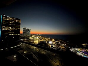 A nighttime cityscape with illuminated buildings, a highway, and a body of water.
