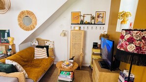Un salon confortable avec un canapé, un pouf, une télévision et une bibliothèque.