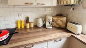 Une cuisine avec des meubles blancs, un plan de travail en bois, une bouilloire, un grille-pain et un dosseret à carreaux.