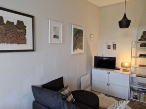 A living room with a sofa, a television on a cabinet, and framed artwork on the wall. - Stylish 1 BDR APT in the heart of Kilmainham (Dublin)