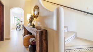 A staircase with a wooden handrail, a white wall with a decorative mirror, and a small table with a vase and candles. - S o Rafael Apartment by Minhos Guest (Albufeira)