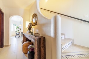 A staircase with a wooden handrail, a white wall with a decorative mirror, and a small table with a vase and candles. - S o Rafael Apartment by Minhos Guest (Albufeira)