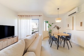 A modern living room with a flat-screen TV, a beige sofa, a dining table with chairs, and a pendant light. - S o Rafael Apartment by Minhos Guest (Albufeira)